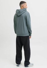 Sweat-shirt à capuche en teal atténué, fabriqué en tissu doux. Présente une coupe décontractée avec un ourlet côtelé, associé à un pantalon noir ample et des chaussures légères.