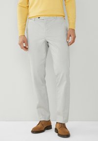 Pantaloni grigi chiari realizzati in tessuto liscio, con una vestibilità a gamba dritta, tasche frontali e una cintura con passanti, indossati con scarpe in suede marrone.