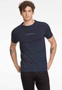 Navy blue cotton t-paita, jossa on lyhyet hihat ja pyöreä kaula-aukko, ja jossa on kevyen sininen "LINDBERGH" -teksti rinnassa.