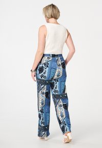 Multicolore broeken met een blauw, zwart en witte paisleyprint, getailleerde pasvorm, hoge taille en zijzakken, gecombineerd met een textuur witte top.