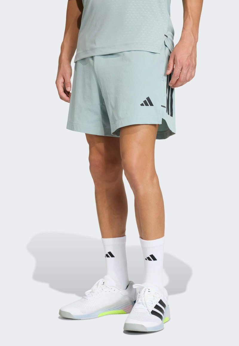 Jasnoniebieskie sportowe spodenki z czarnymi logo adidas, noszone z białymi skarpetami z czarnymi paskami. Kompozytowy materiał, luźny krój z bocznym rozcięciem.