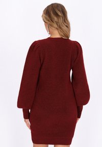 Burgundy-neulakjole med teksturstoff, lange pufferm, og ribbet kant. Enkel rund hals, kne-lengde design.