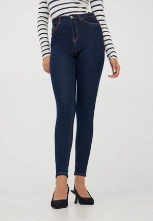 Ciemnoniebieskie, wysokie dżinsy z denimu, z klasycznym pięcio-kieszeniowym krojem i kontrastowym szyciem, zestawione z czarnymi szpilkami.