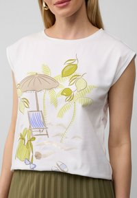 Weiße Kurzarmbluse mit einem Strandmotiv, das Palmen, Zitronen, einen Sonnenschirm und einen gestreiften Stuhl zeigt. Aus weichem Baumwollmaterial.