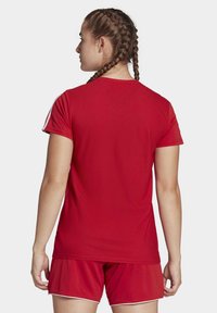 Maglia sportiva rossa con un motivo testurizzato e maniche corte, caratterizzata da dettagli bianchi sulle spalle. Indossata con pantaloni corti rossi.