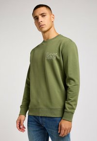 Sudadera verde oliva hecha de tela suave, con un cuello y puños acanalados, y el logo "Lee" bordado en el pecho.