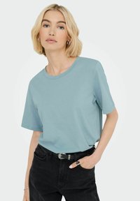 Lys blå bomulds T-shirt med korte ærmer og en rund halsudskæring, parret med sorte bukser. Har en afslappet pasform og glat tekstur.