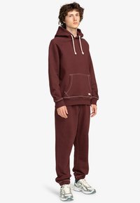 Bordeaux hoodie en sweatpants set gemaakt van zachte stof. De hoodie heeft een voorzak en een trekkoord, terwijl de joggers elastische manchetten hebben.