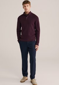 Bordeaux gebreide pullover met een kraag en knoopdetails, gecombineerd met donkerblauwe getailleerde broek en tan sneakers. Soepele textuur, getailleerd ontwerp.