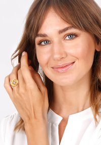 Gold ring with a central blue stone, round shape, polished finish, worn on the right hand. Model wearing a white top and smiling.
