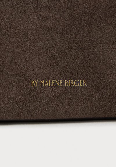Καφέ σουέντ υλικό με απαλό υφή που διαθέτει το ανάγλυφο κείμενο «BY MALENE BIRGER» σε χρυσό χρώμα. Απλός, ορθογώνιος σχεδιασμός.