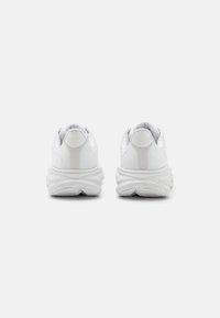 Zapatillas blancas con un upper de tela texturizada, punta redondeada y suela gruesa con patrón en onda. El logotipo y los detalles están estampados en la parte trasera.