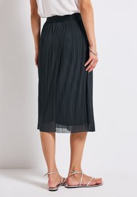 Black pleated midi skirt with a textured fabric and elastic waistband, paired with silver strappy sandals, showcasing a flowing design.