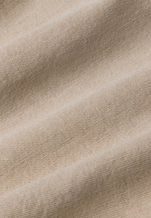 Gros plan d’un tissu beige avec un motif de tissage diagonal fin et des plis doux.