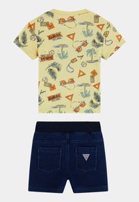 T-shirt jaune à manches courtes avec imprimé tropical, associé à un short en denim bleu foncé, doté d'une taille élastique et de deux poches arrière.