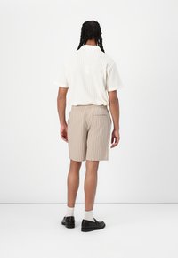 En tekstureret hvid polo med korte ærmer, parret med beige shorts med striber. Sorte loafers og hvide sokker fuldender outfittet.