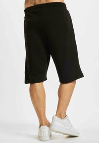 Black cotton sweat shorts with an elastic waistband, hemmed cuffs, and side pockets, paired with white sneakers.
