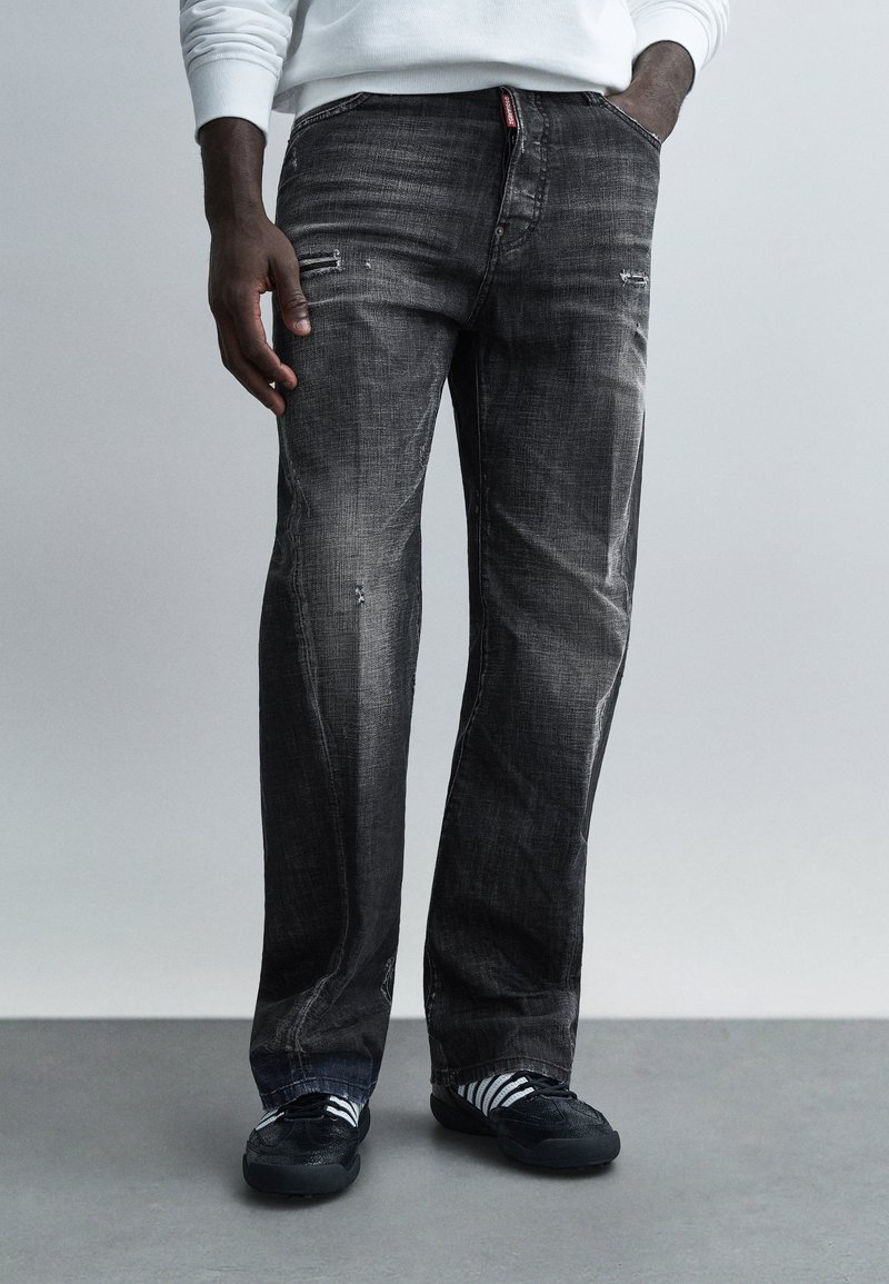 Black denim jeans with a straight-leg fit. Features distressed accents, faded texture, and front pockets. Worn with black sneakers and striped socks.