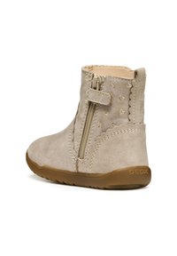 Botín de ante beige hasta el tobillo con cremallera lateral, acentos de corazón dorado, bordes con ondas y suela de goma flexible. Logo de la marca en el talón.