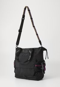 Musta kangaskassi, jossa on kahdet kahvat, säädettävä olkahihna, verkkotasku sivulla ja vetoketjut yksityiskohdissa. Koristeena kuvioitu hihna.