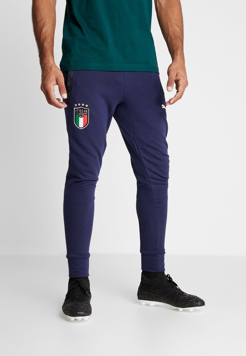 Marineblauwe sportbroek met een aansluitend ontwerp, voorzien van een geborduurd Italiaans vlaglogo op de dij en gouden accenten. Het materiaal lijkt zacht en rekbaar.