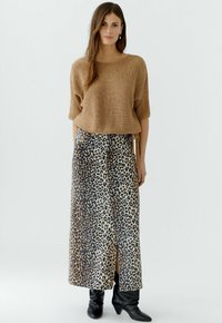 Brauner gestrickter Crop-Pullover kombiniert mit einem langen Rock im Leopardenmuster, der einen seitlichen Schlitz hat. Schwarze Stiefeletten vervollständigen das Outfit.