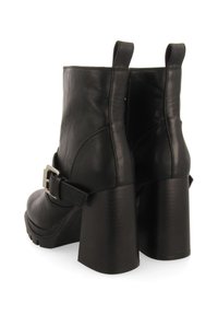 Botas de tobillo de cuero negro con un alto tacón cuadrado, tiradores traseros y un acento de hebilla en el lateral. Textura suave con un acabado brillante.