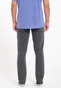Jeans de mezclilla gris, corte recto, con una textura ligeramente desgastada. Llevados con una camisa azul clara, combinados con unas zapatillas Converse blancas.