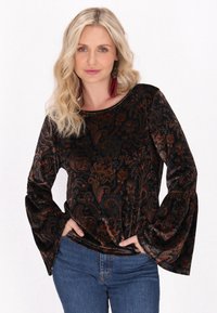 Černý sametový top s paisley vzorem, kulatým výstřihem a rozšířenými dlouhými rukávy. Nosený s modrými džínami.