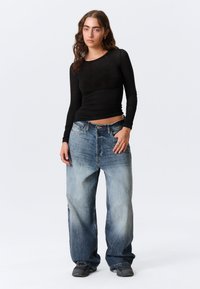 Top nero a maniche lunghe abbinato a jeans di denim blu larghi con effetto sbiadito. L'outfit è completato da scarpe da ginnastica grigie.