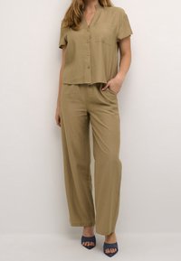 Completo in due pezzi khaki composto da una camicia a maniche corte con bottoni e tasca, abbinata a pantaloni larghi; tessuto morbido e testurizzato con una vestibilità comoda.