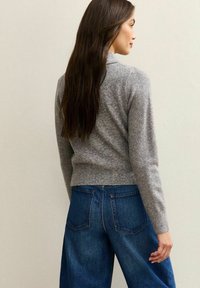 Grå tröja med strukturstickning, tight vid midjan, tillsammans med lösa blå denimjeans med bakfickor och hög midja.