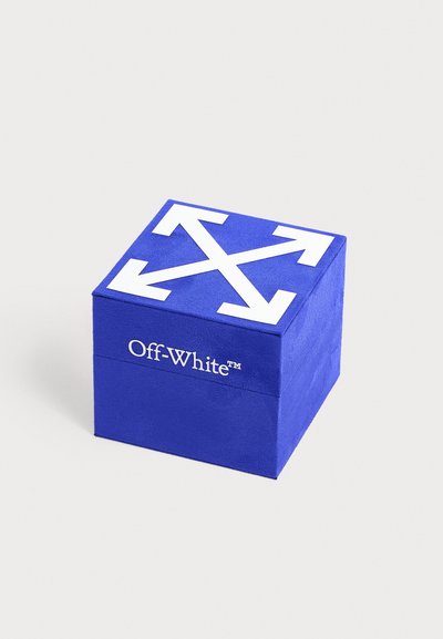 Boîte carrée bleue avec des flèches blanches croisées en haut et texte "Off-White" sur le côté, sur un fond clair.