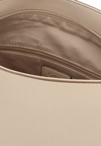 Beige Handtascheninnenteil mit einer glatten, lederähnlichen Textur. Enthält eine Reißverschlusstasche und einen Stofffutter mit einem subtilen Glanz.