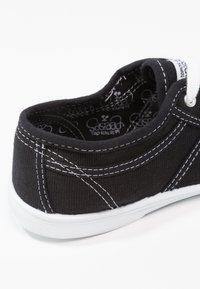 Sneaker nera in tela con cuciture bianche e suola in gomma. Presenta un tacco arrotondato e una fodera interna testurizzata. Lacci nella parte frontale.