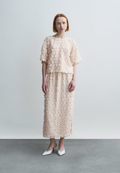 Ensemble deux pièces orné de fleurs, de couleur pêche clair, comprenant un haut ample et une longue jupe à texture lisse et tombé doux. Escarpins blancs élégants.