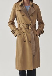 Khaki trenčkot s dvořadými knoflíky, opaskem v pase a podšívkou v houndstooth vzoru na límci. Hladká textura, přiléhavý střih.