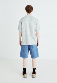 Chemise grise à manches courtes, shorts en denim, chaussettes noires et baskets multicolores. Design simple, coupe décontractée et texture douce.