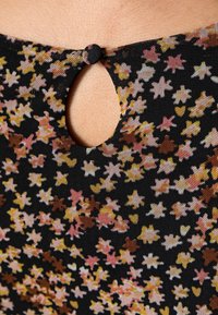 Sorte stof med et blomstermønster i pink, gul og orange. Har en nøglehulåbning bagpå, sikret med en knap.