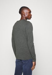 Camicia a maniche lunghe verde scuro realizzata in tessuto testurizzato, con scollo rotondo e vestibilità comoda, abbinata a jeans blu.