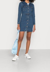 Denim-paita mekko pitkilla hihoilla, nappikiinnitys edessä, kaksi etutaskua ja vyöllinen vyötärö. Yhdistetty vaaleansinisellä sitruunapussilla ja valkoisilla lenkkareilla.