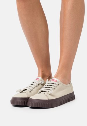 Beiga canvas-sneakers med bruna gummisula, rund tå och snörningsdesign. Har en liten röd logotagg på tungan.