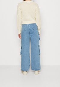 Krämfärgad stickad tröja kombinerad med ljusblå vida cargobyxor med sidofickor. Chunkiga krämfärgade platåskor fulländar looken.