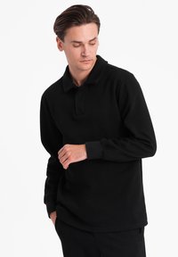 Sort langærmet polo skjorte lavet af bomuld. Har en klassisk krave og ribbede manchetter, med en afslappet pasform og uden synlige mønstre.