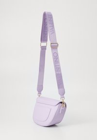 Lila crossbody torba s zakrivljenim oblikom, glatkom teksturom i magnetskim poklopcem. Ima teksturiranu lavandu traku s utisnutim "Valentino".