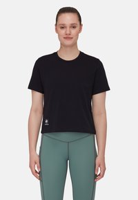 Fekete, rövid ujjú, rövid fazonú póló, kerek nyakkivágással. Bal alsó sarkán egy kis logós patch található. Zöld leggingsszel párosítva.