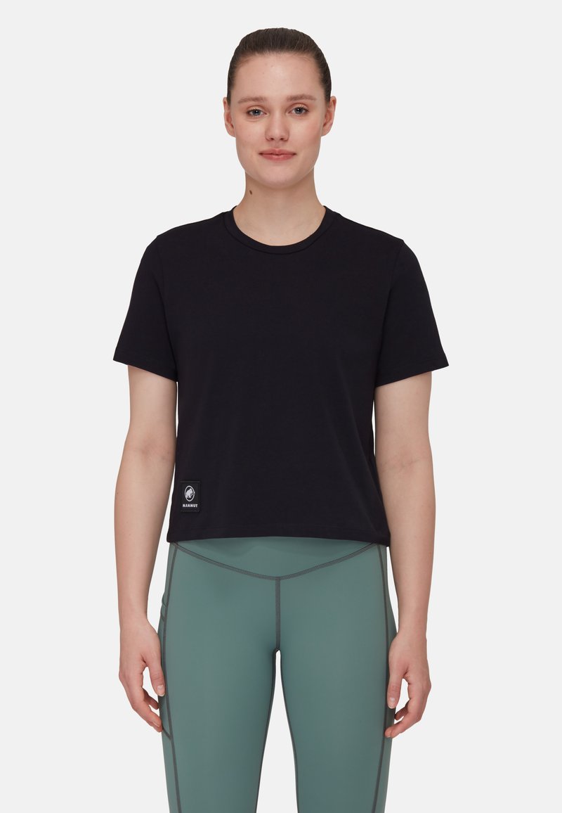Fekete, rövid ujjú, rövid fazonú póló, kerek nyakkivágással. Bal alsó sarkán egy kis logós patch található. Zöld leggingsszel párosítva.