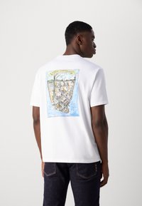 Hvid bomulds t-shirt med et farverigt illustreret kort over Nieuw Amsterdam på ryggen, med et gult banner der detaljerer placeringen.