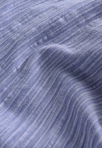 Tissu bleu clair avec un fin motif rayé, présentant des textures alternées. Doux et légèrement brillant avec une texture lisse.