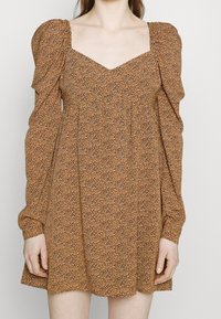 Robe marron à motifs avec manches ballon, encolure carrée, coupe décontractée et texture douce. Le tissu présente un petit motif animalier foncé.